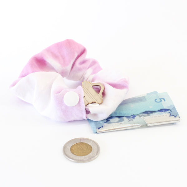 purple and white tie dye scrunchie with a snap open pocket to store your goodies in- scrunchie pictured has a key in the pocket and money beside it. white background.