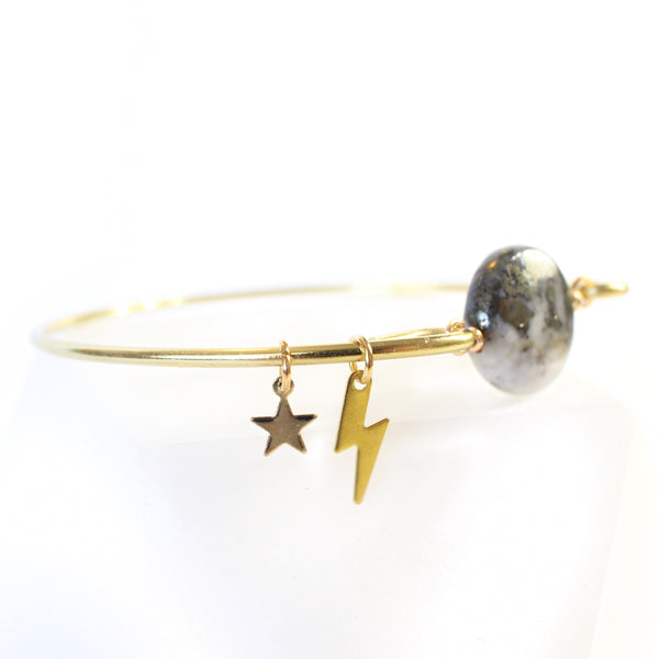 gold wire bangle with two sides held together with a pyrite and quartz coin shaped bead. there are little gold charms on the bangle, a star and a lightning bolt. the pyrite on the bead resembles the marbling on a planet. 45 degree view, showing the charms, white background.