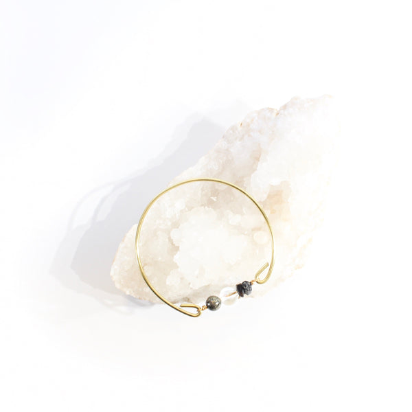 gold brass bangle with pyrite, quartz and black tourmaline beads laying on a crystal bed  with white background