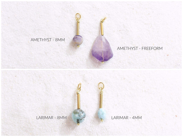 split photo- top- white sand with gold + amethyst pendants laid on top- one is an 8mm sphere, the other is a faceted freeform shape. bottom- white sand with Larimar nugget pendants laid on top- freeform nugget shape, one is 8mm, the other is 4mm