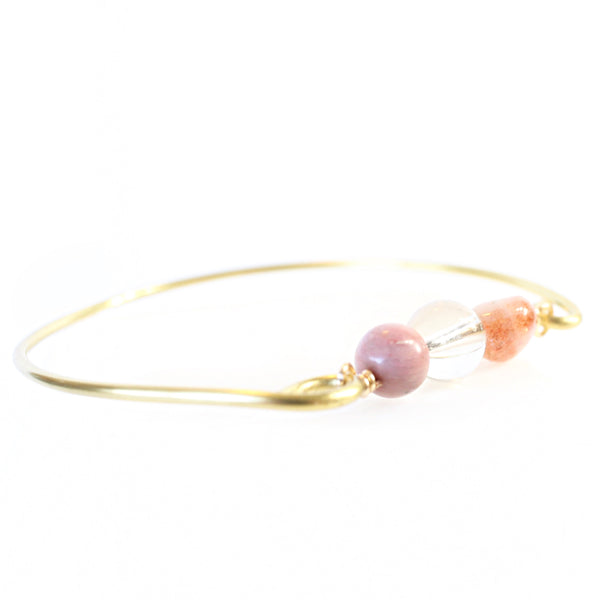 gold wire bangle with two sides held together by rhodonite, clear quartz and sunstone beads. 45 degree angle view,  white background