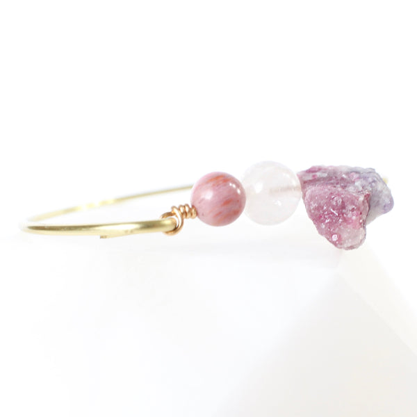 gold bangle with rhodonite, rose quartz and pink tourmaline beads in the middle. photo is taken at a 45 degree angle from the crystals and there is a white background