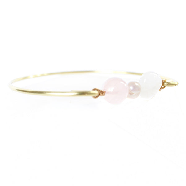 gold brass bangle with rose quartz, pearl and moonstone beads in the middle. white background.  45 degree angle shot.