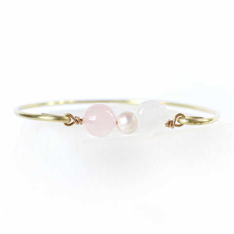 gold brass bangle with rose quartz, pearl and moonstone beads in the middle. white background.