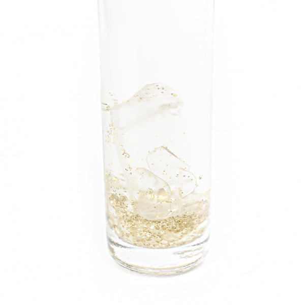 white background with a clear glass roller bottle with a black lid. the bottle has a holographic Gem+Aura logo. in the roller is clear quartz and gold glitter