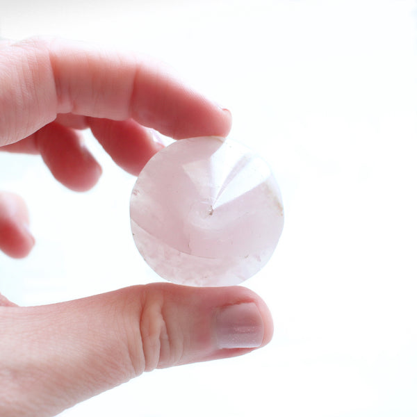 1.5 - 2 inch diameter cone shaped rose quartz specimen. cone is being held between the thumb and forefinger of a caucasian woman, with a white background