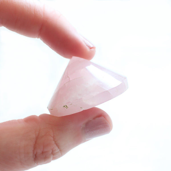 1.5 - 2 inch diameter cone shaped rose quartz specimen. cone is being held between the thumb and forefinger of a caucasian woman, with a white background