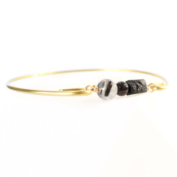 Gold bangle with raw black tourmaline, a small garnet, and a tourmalinated quartz bead with a white background