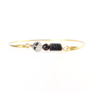 Gold bangle with raw black tourmaline, a small garnet, and a tourmalinated quartz bead with a white background