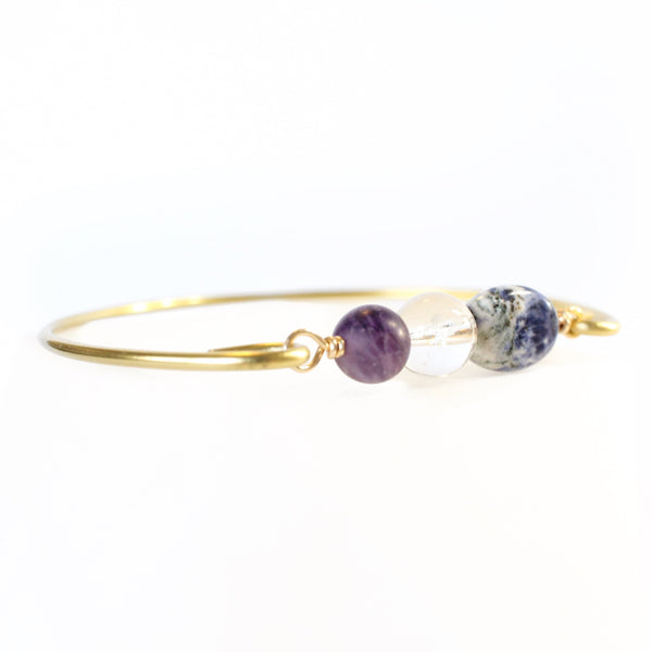 gold coloured bangle with amethyst, clear quartz and sodalite beads connecting the two sides of the wire bangle. white background, close up 45 degree view.