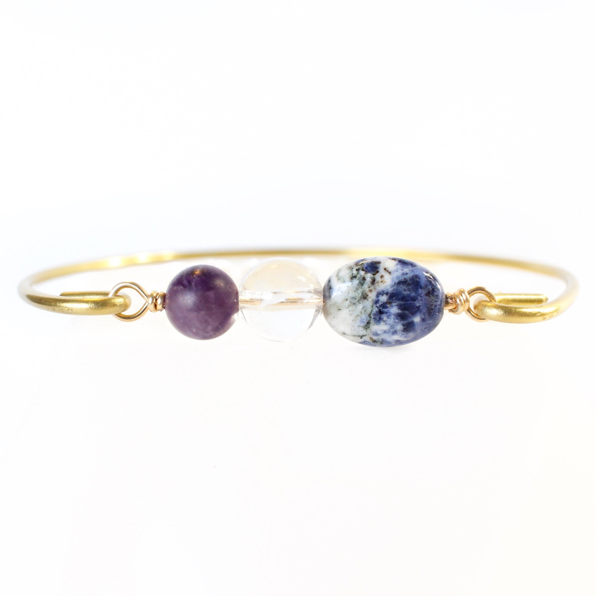 gold coloured bangle with amethyst, clear quartz and sodalite beads connecting the two sides of the wire bangle. white background, close up front view.