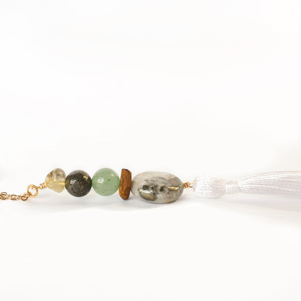 string of crystals with a loop of thin gold chain to hang it. the crystals from top to bottom are citrine, pyrite, green aventurine, tigers eye and pyrite in quartz. at the bottom to the crystals is a white tassel. white background.