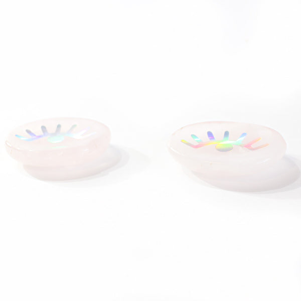 rose quartz eye discs sitting on a white background. photo is taken from a front view, showing thickness of discs. eye discs have holographic decals of an eye with eyelashes.