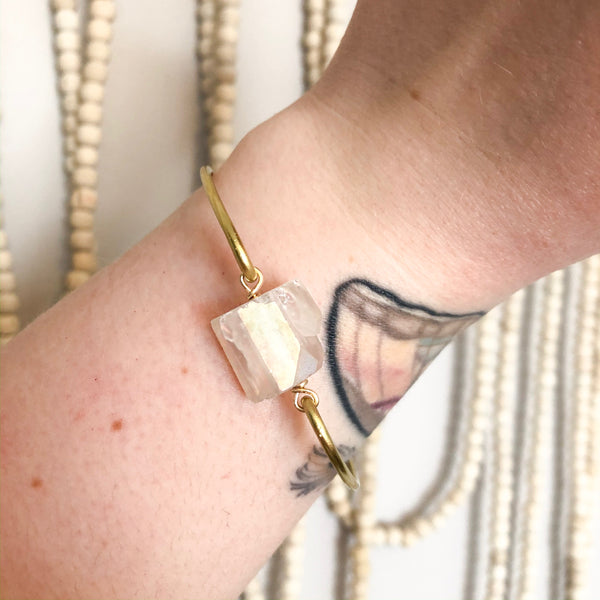 gold bangle with an aura quart chunk on it shown worn on a caucasian woman's tattooed wrist.