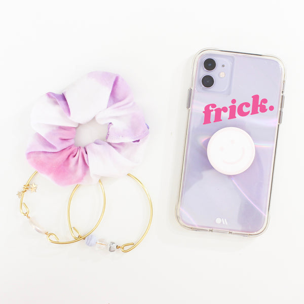 flat lay image of a purple iPhone, a scrunchie and two gold bangle bracelets.  on the phone case, there is a hot pink decal that says Frick in a chunky retro font.