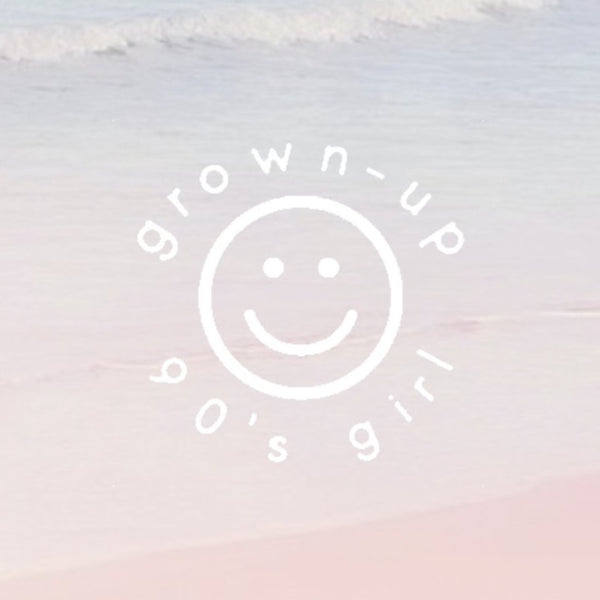 white circled happy face with "grown-up 90's girl" written around the circle in a simple font. background is a faded ocean view