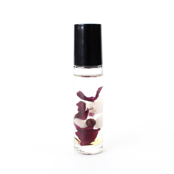 clear glass roller bottle with a black lid, in the bottle is an essential oil blend with dried rose petals, rose quartz, garnet and clear quartz inside. there is a white background