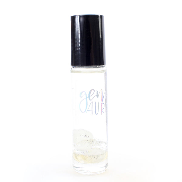 clear glass oil roller bottle with a black lid. It has a holographic Gem + Aura logo on it. The bottle is filled with oil and in it there is clear quartz, moonstone, and mother of pearl with silver glitter. white background
