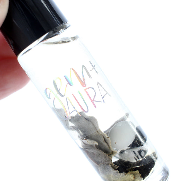 white background, clear glass oil roller bottle with a black lid. inside is dried sage, cats eye, black tourmaline and tourmalinated quartz in an oil blend. There is a holographic gem and aura logo on the bottle.