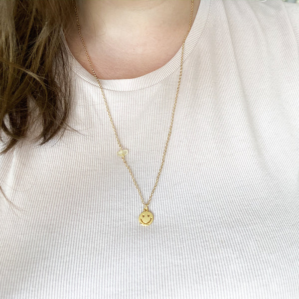 gold smiley face pendant on a dainty gold chain with a little piece of citrine on the chain. necklace is shown modelled on a caucasian woman with brown hair