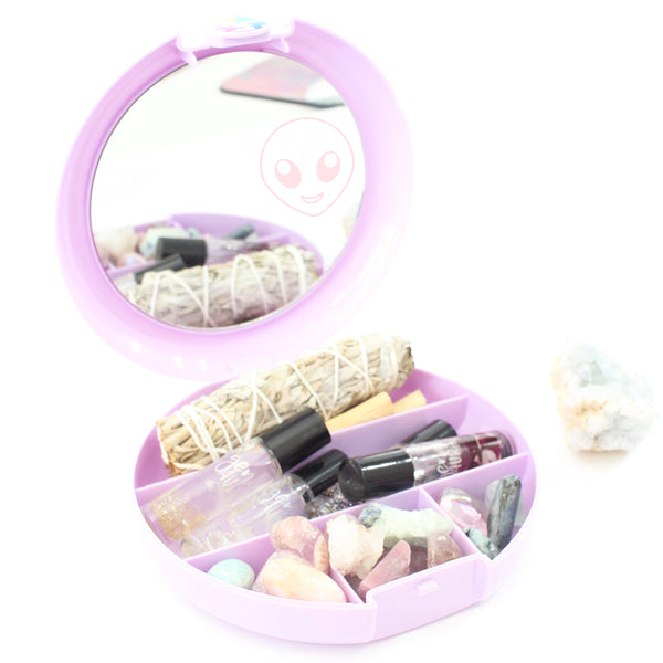 purple circular caboodles case filled with crystals, oil rollers, sage wand and palo Santo. the case is open and there is a mirror on the lid. the mirror has a pink emoji-style alien head decal on it