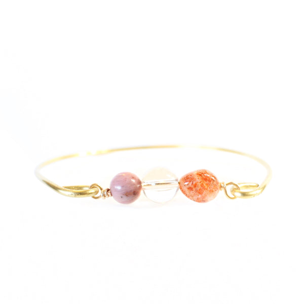 gold wire bangle with two sides held together by rhodonite, clear quartz and sunstone beads. close up front view, white background