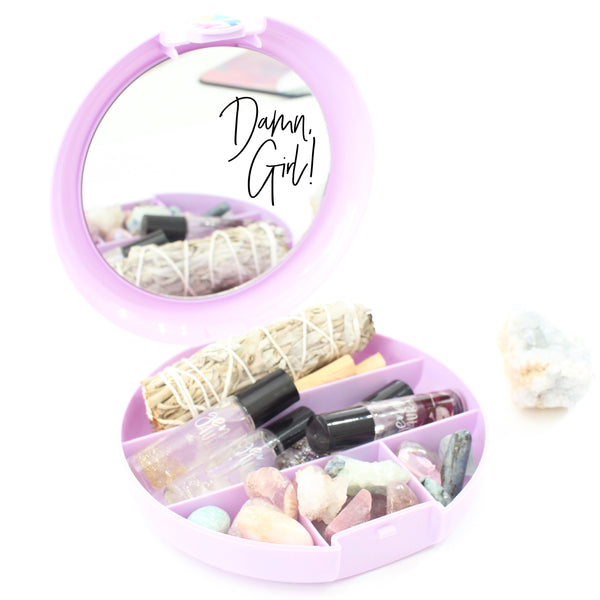 white background with a purple caboodles case filled with crystals, roller balls, sage and palo Santo. on the mirror of the case there is a black Damn Girl decal