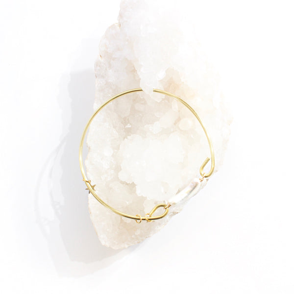 gold bangle with a moon shaped freshwater pearl in the middle. there are three little gold star charms on the bangle. white background, top view, bracelet is laying on a bed of white crystal clusters