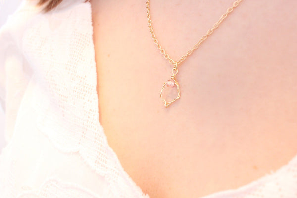 close up gold wire yoni charm on a 22" dainty gold chain, worn by caucasian woman in white shirt