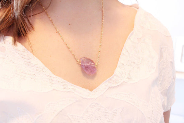 large raw amethyst chunk on 22" thin gold chain, modelled by a caucasian woman with shoulder length brown hair wearing a white shirt. 