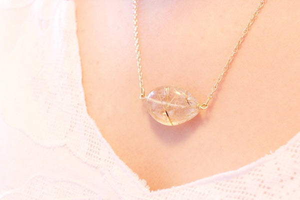 close up of gold rutilated quartZ necklace worn by caucasian woman in white shirt