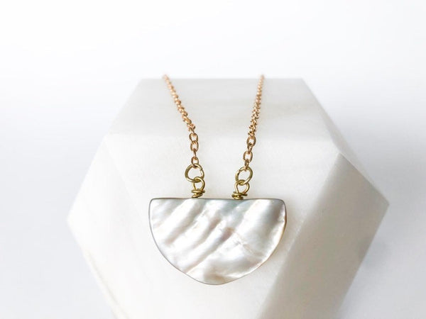 birds eye view: silvery iridescent half moon shaped seashell pendant on a geometric marble decor. white background