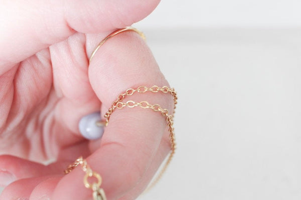 caucasian woman hand holding healing charm attached to dainty gold chain, holding over white sand