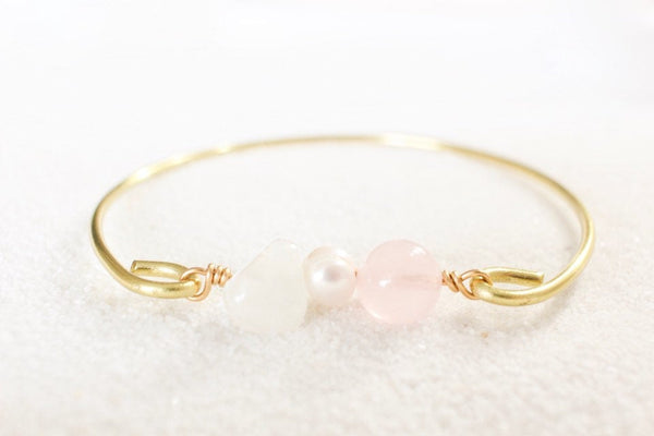 gold brass bangle with moonstone, pearl and rose quartz beads, front view laying on white sand