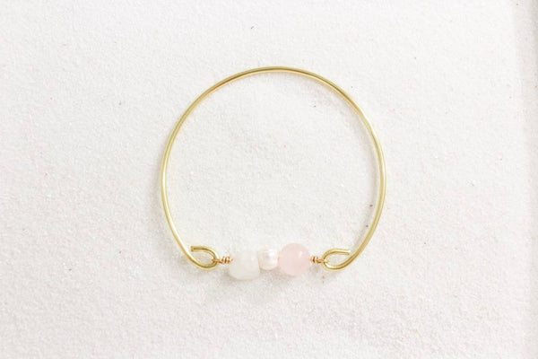 gold brass bangle with moonstone, pearl and rose quartz laying on white sand