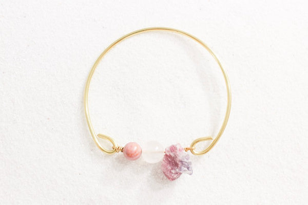 top view of self love bangle- gold brass with rhodonite, rose quartz, and pink tourmaline beads. laying on white sand