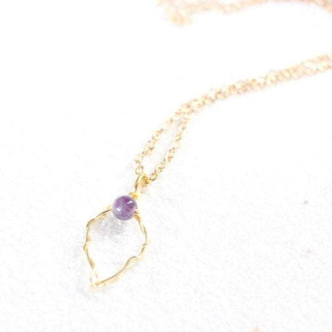 gold wire yoni with gemstone clitoris on a dainty gold chain, laying on white sand