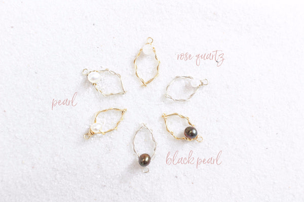 6 wire yoni charms in silver and gold with different gemstone clitorises of rose quartz, black pearl, and pearl. in a circle laying on white sand