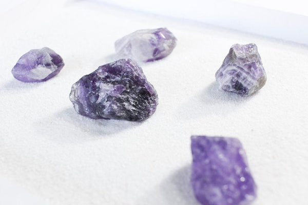 deep purple raw amethyst chunks laying on white sand, to show different shapes and sizes 