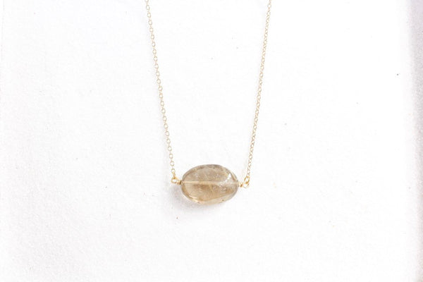 top view of gold rutilated quartz necklace laying on white sand