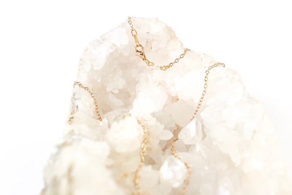 dainty gold chain laid on quartz geode cluster. chain has a small quartz bead by the clasp. white background