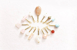 moonstone, unakite, larimar, carnelian, pearl, and rose quartz pendants, all with gold detail, laying in a sunburst shape on white sand