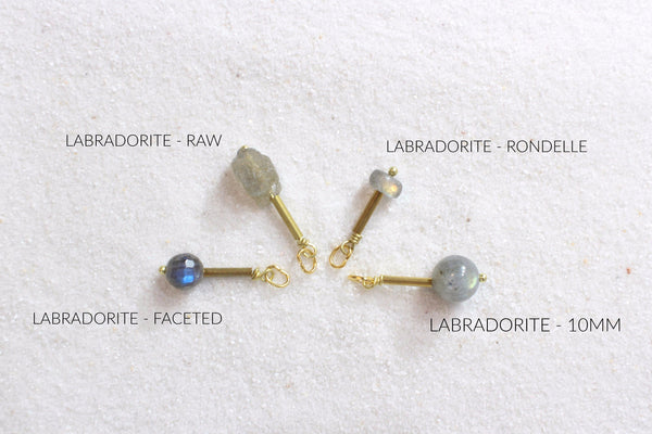 labradorite pendants with gold brass detail laid out on white sand