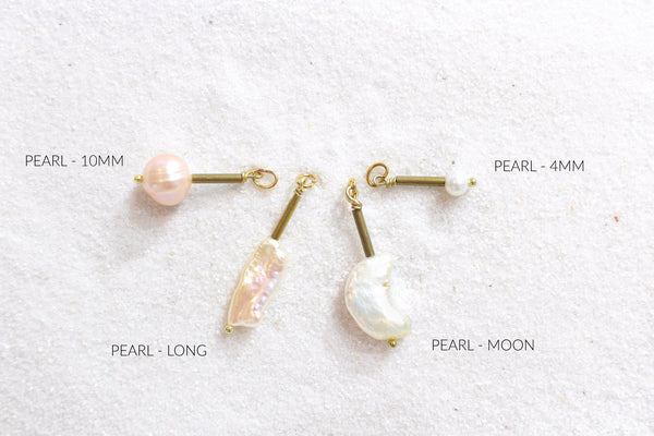 large pink pearl, long pink pearl, moon shaped pearl, and tiny pearl pendants laying on white sand