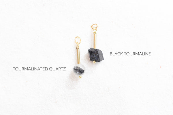 tourmalinated quartz and black tourmaline pendants with gold brass detail laying on white sand