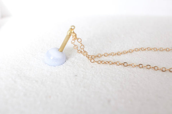 blue lace agate healing pendant strung onto thin gold chain, sitting in white sand