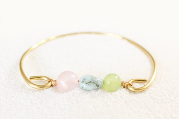 gold brass bangle bracelet with rose quartz, larimar and jade beads. front view, laying on white sand