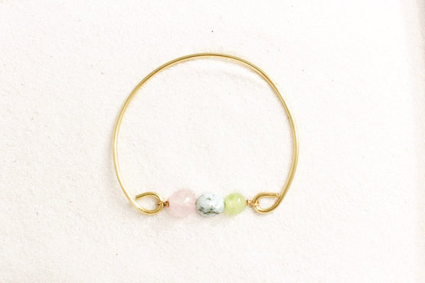 gold brass bangle with rose quartz, larimar and jade beads. top view, laying on white sand