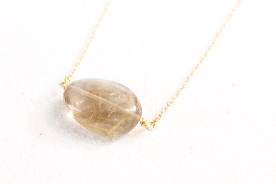 45 degree angle view smokey gold rutile quartz necklace laying on white sand