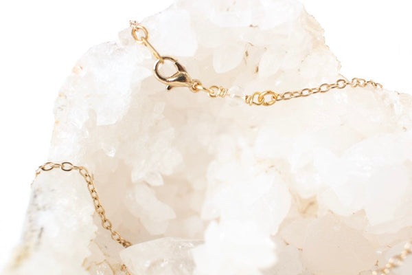 close up of thin gold chain over quartz geode, clasp is shown with a small quartz bead on it. white background